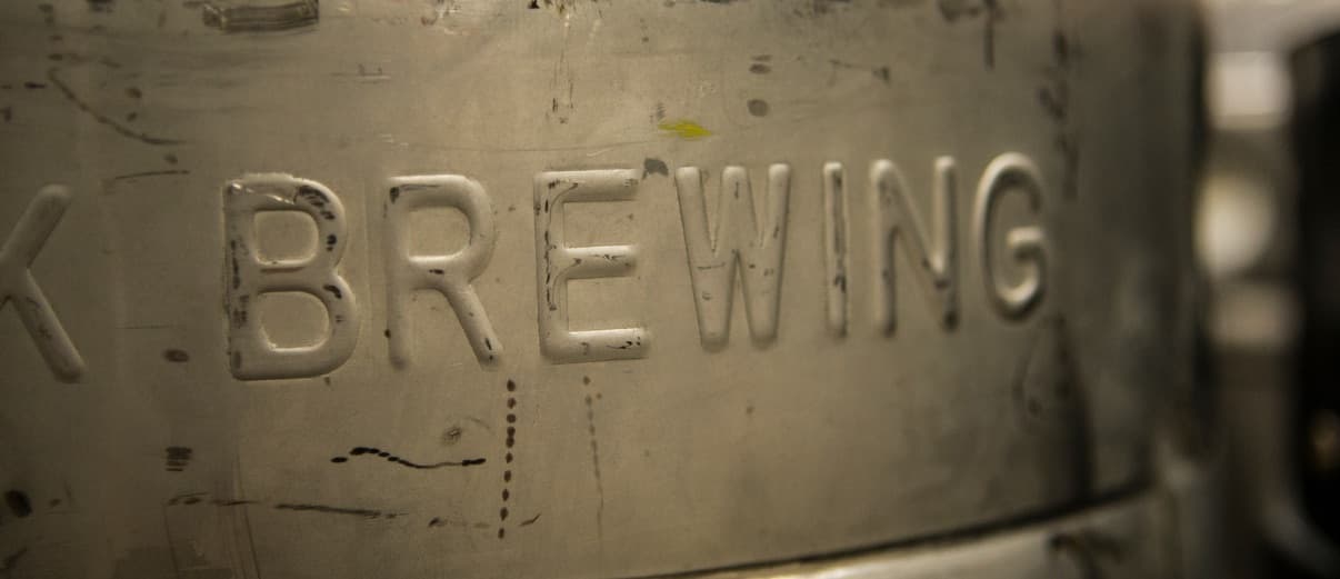 Close-up of a stainless steel brewing vessel with BREWING embossed in the metal surface