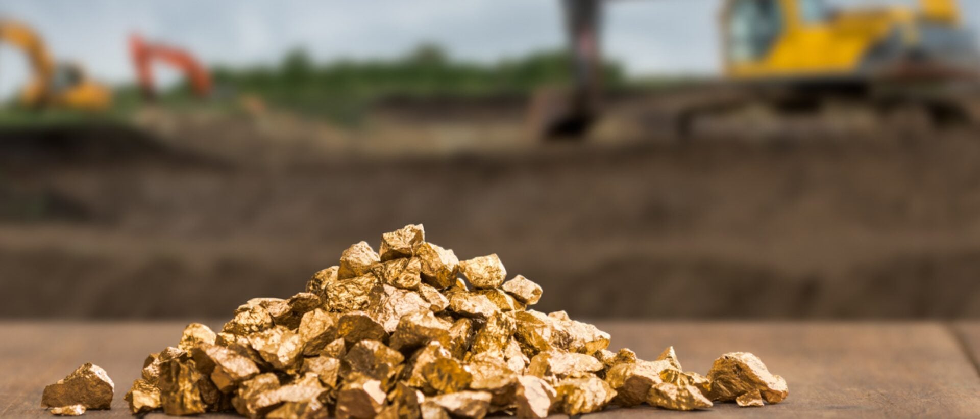 Pile of gold nuggets at an open-pit mining site with excavators in the background — representing the gold recovered using activated carbon in CIP, CIL and CIC adsorption circuits