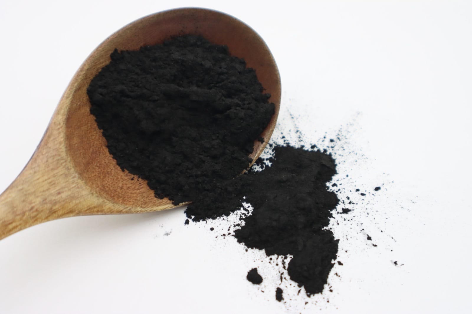 Wooden spoon heaped with fine black powdered activated carbon on a white surface — food-grade decolorizing agent for citric acid purification
