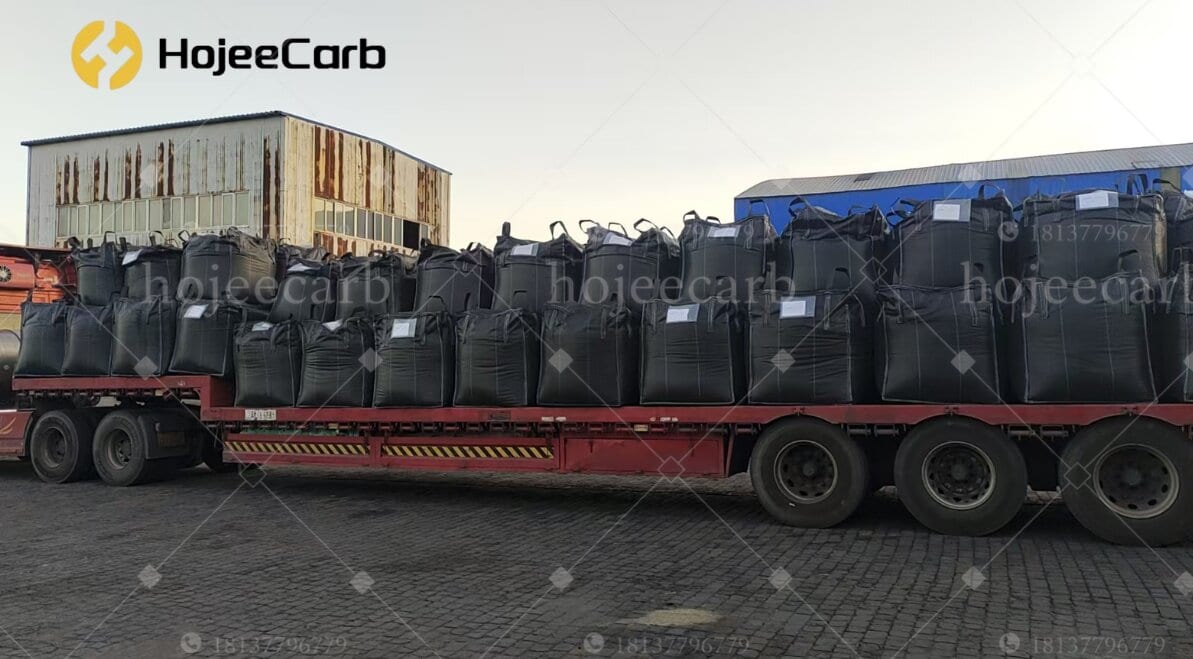 Dark charcoal-black FIBC jumbo bags of activated carbon stacked and loaded on a red flatbed truck parked beside a warehouse — HojeeCarb bulk export shipment